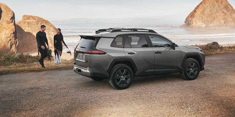 Toyota RAV4 SUV parked near a rocky coastline with two people standing beside it.