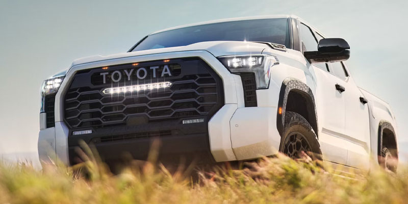White Toyota Tundra pickup truck driving through grassy terrain.